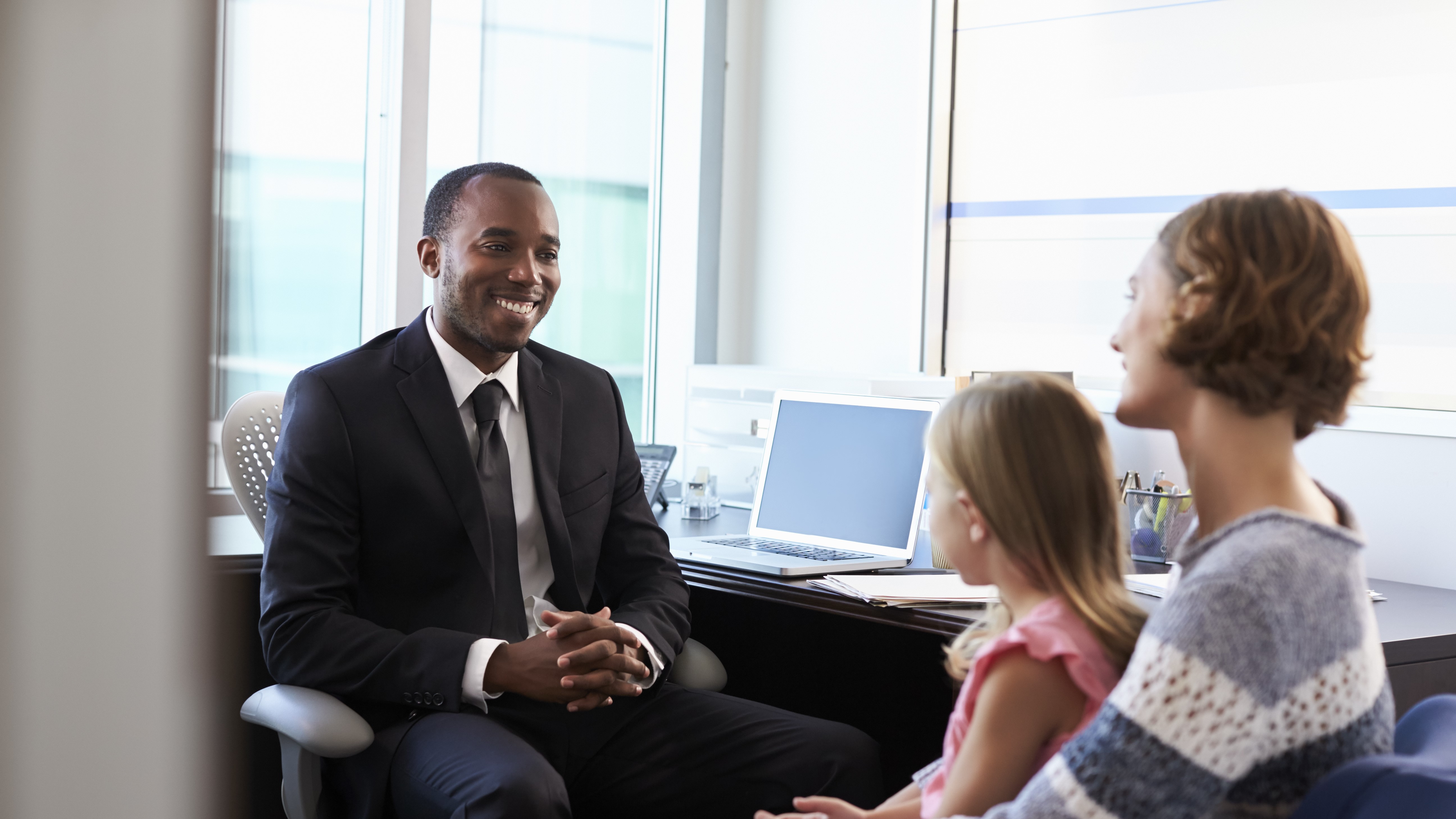 Photo of adult male in professional business suit sitting and smiling meeting with a mother and her daughter sitting in her lap